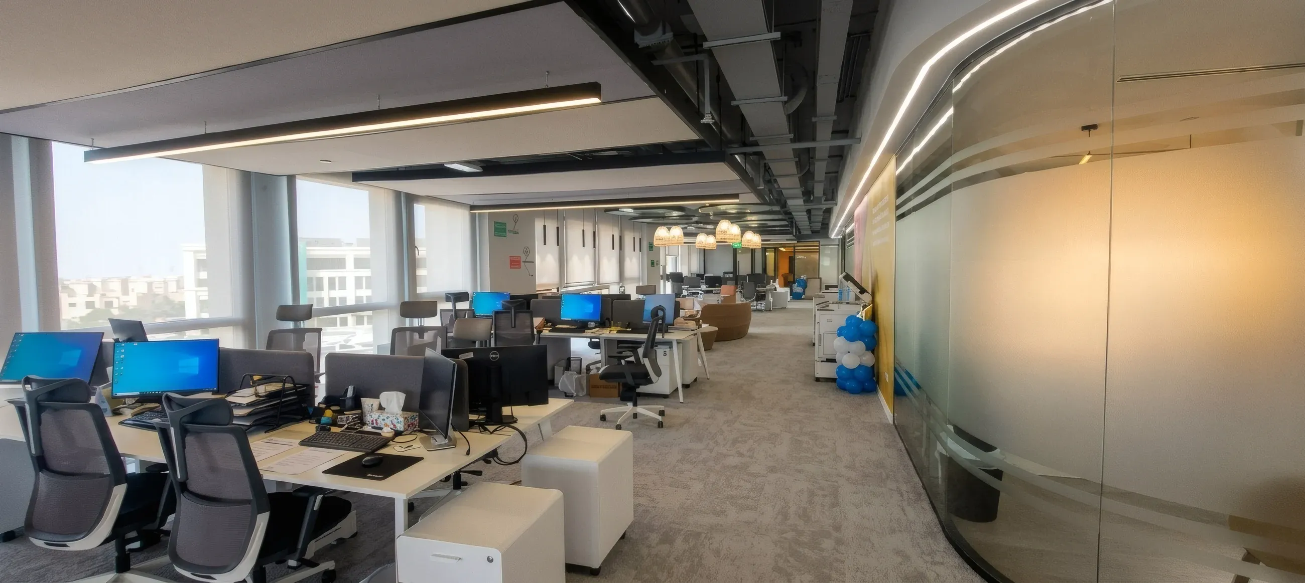 Open-plan office with white desks beside a frosted glass partition