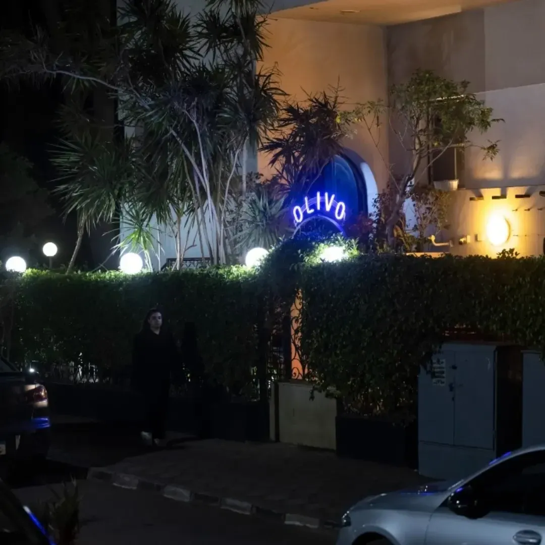 Olivo entrance at night with a blue neon sign behind hedges