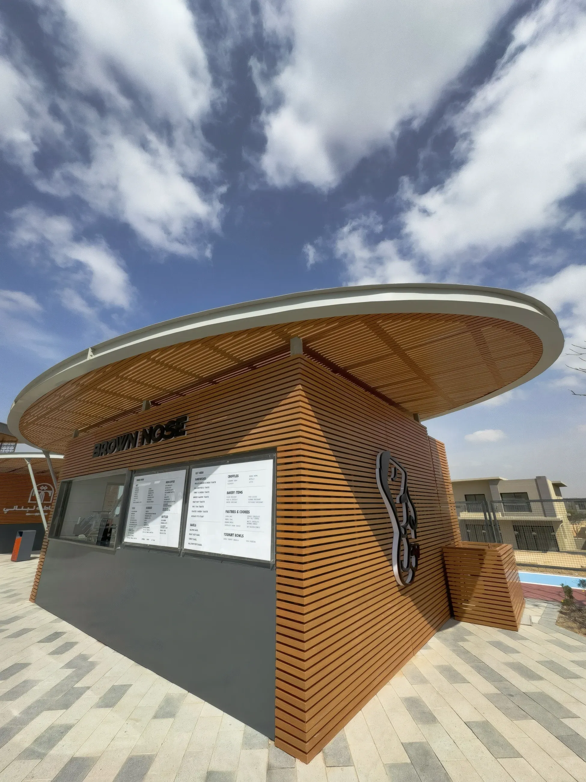 Round-roofed timber slat kiosk with menu boards under a cloudy sky