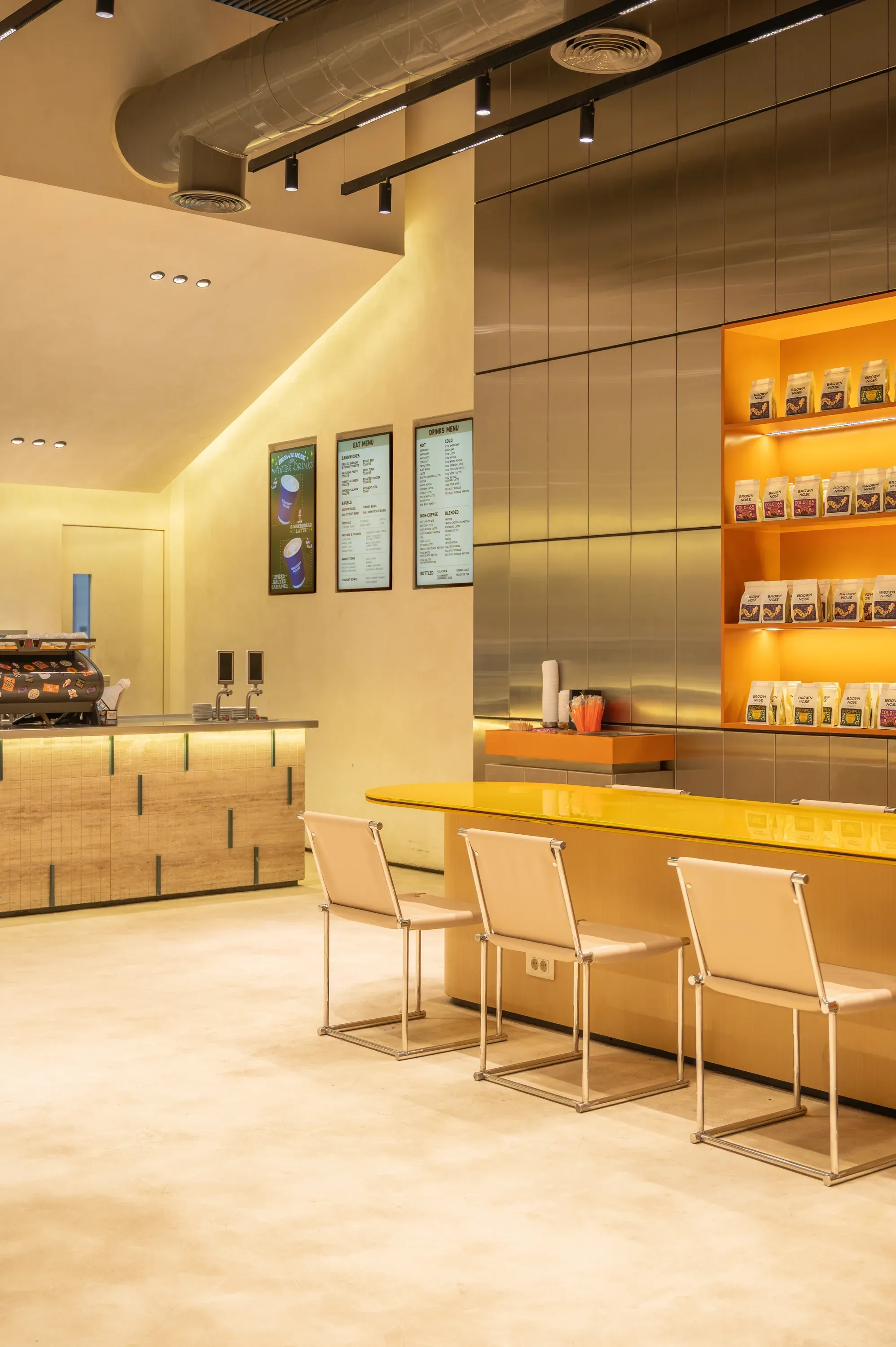 Yellow counter and chairs in front of a brushed steel wall with orange shelves