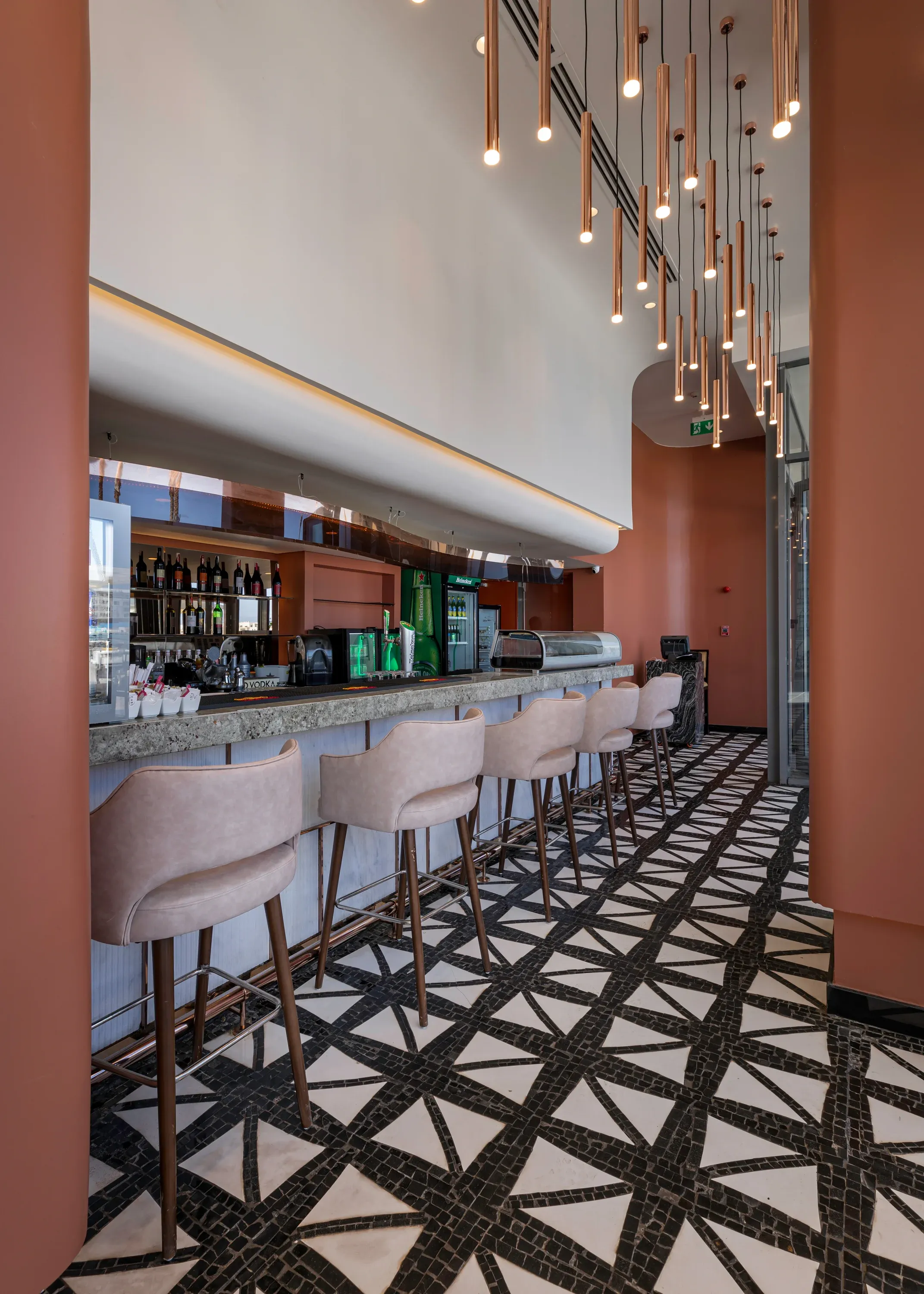Bar with pink-cushioned stools and terracotta column under hanging copper lights