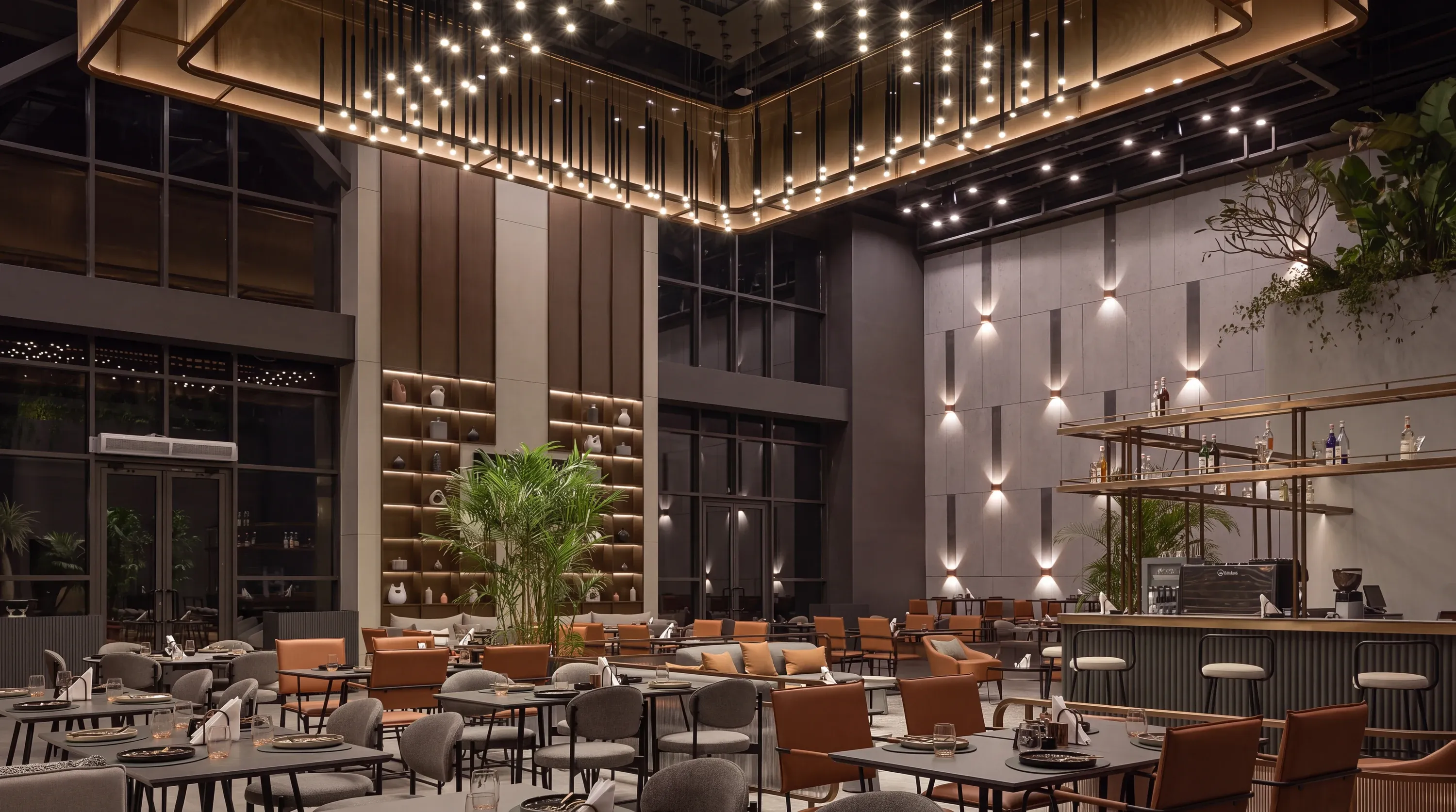 Dining hall under a lit brass ceiling canopy with planters and bar