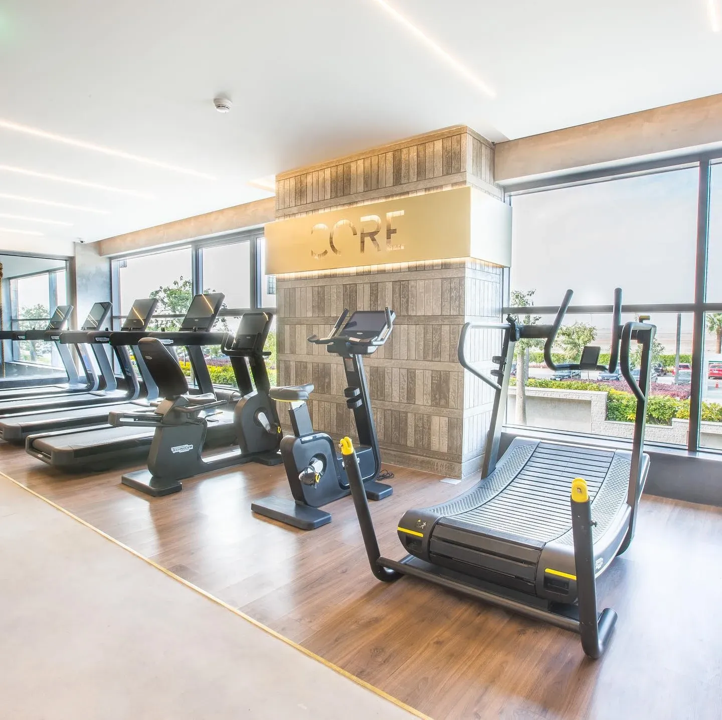 Cardio machines along the window beside a timber floor and Core sign