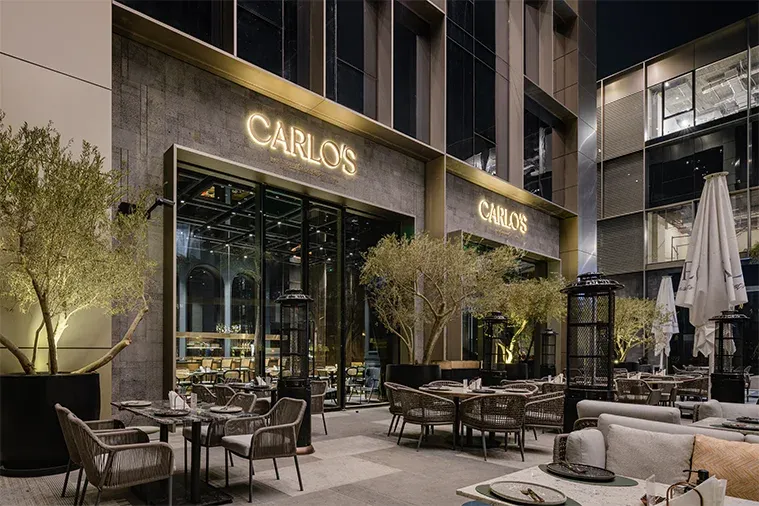 Carlo's entrance and terrace with olive trees and outdoor tables at night