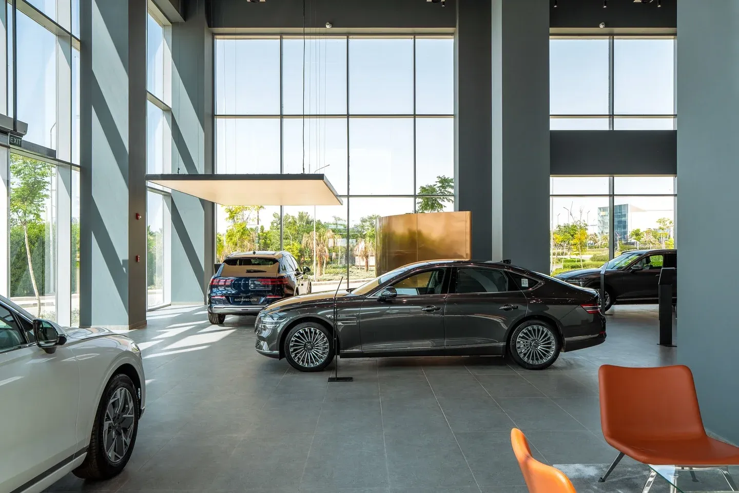 Showroom hall with floor-to-ceiling glazing, a dark sedan and orange chairs