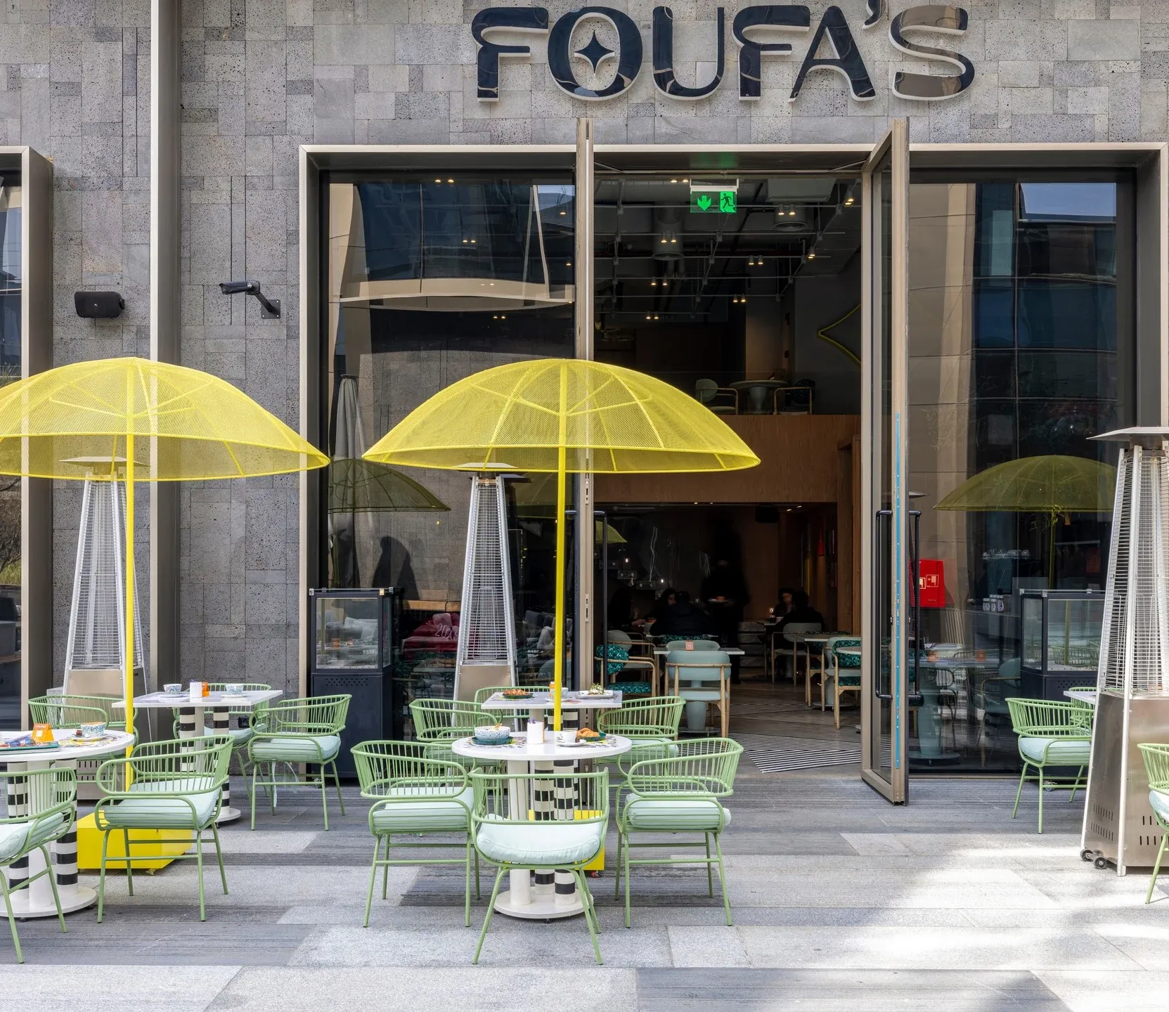 Foufa's entrance with yellow umbrellas and green terrace chairs