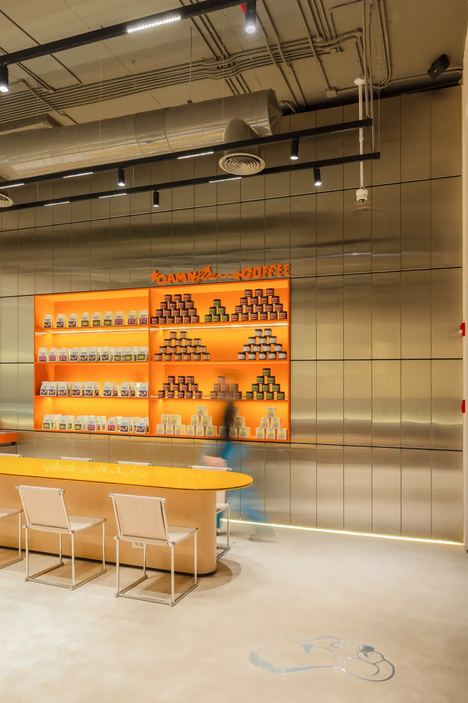 Brushed steel wall and orange shelving display under exposed ceiling services