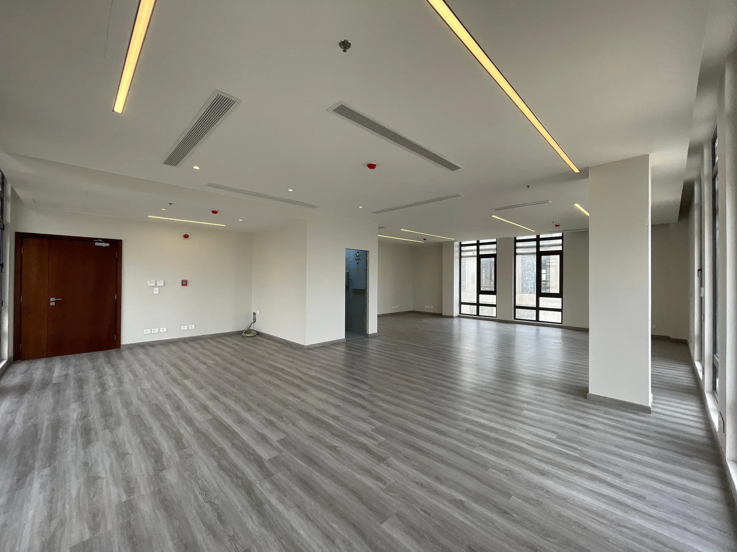Empty office floor with grey plank flooring, tall column and linear ceiling lights