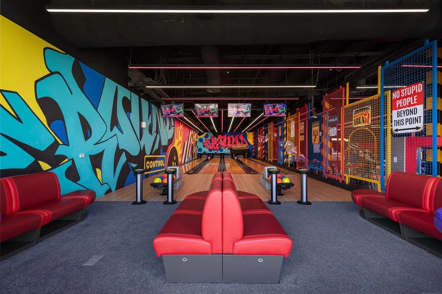 Red banquette seating facing the graffiti mural and bowling lanes, wider view
