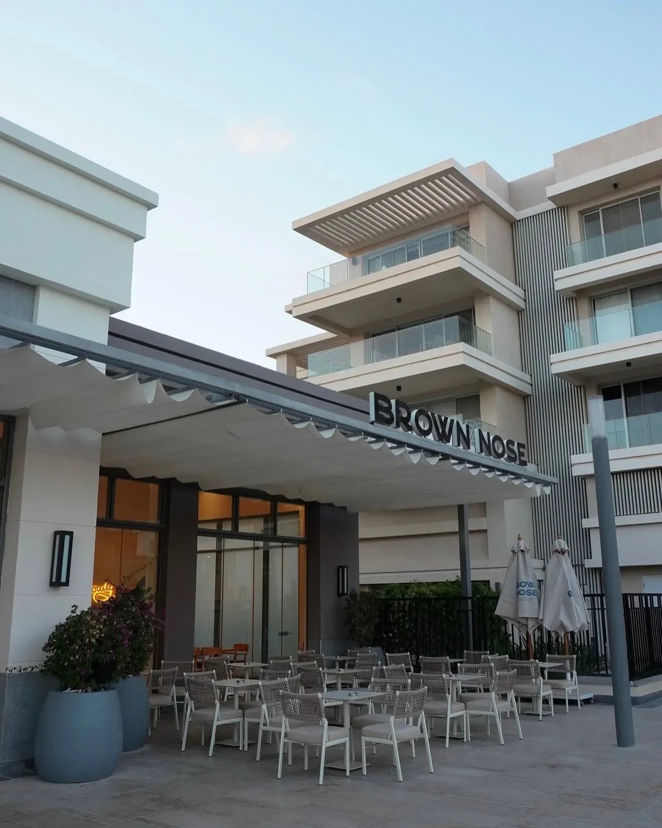 Brown Nose canopy and white terrace chairs beside an apartment block