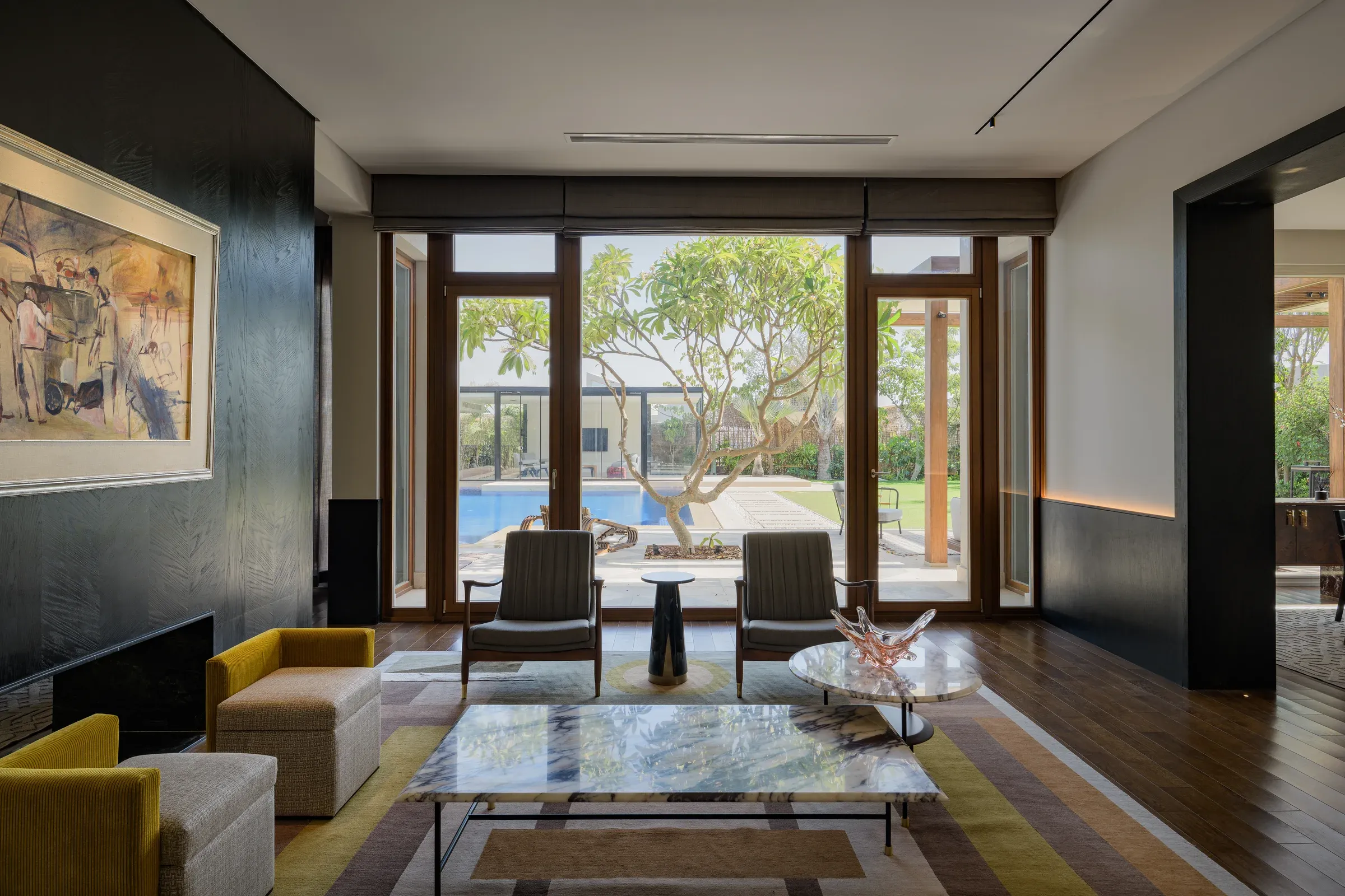 Framed painting on a black wall above a marble coffee table and yellow armchairs