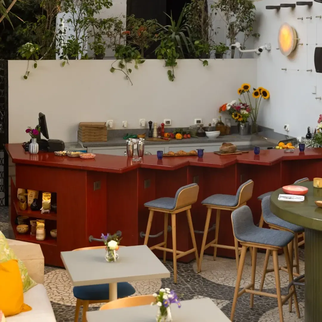 Red-fronted bar counter with timber stools and flowers in the courtyard