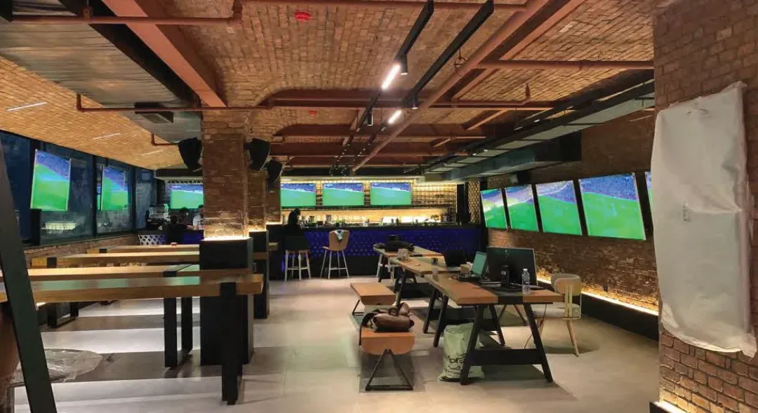 Sports bar hall with long timber tables, brick vaulted ceiling and screens