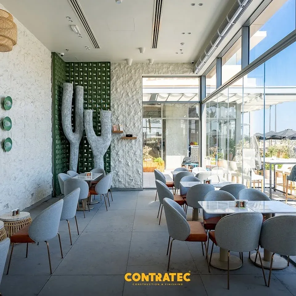 Grey chairs and marble tables along the glass wall, textured wall at left