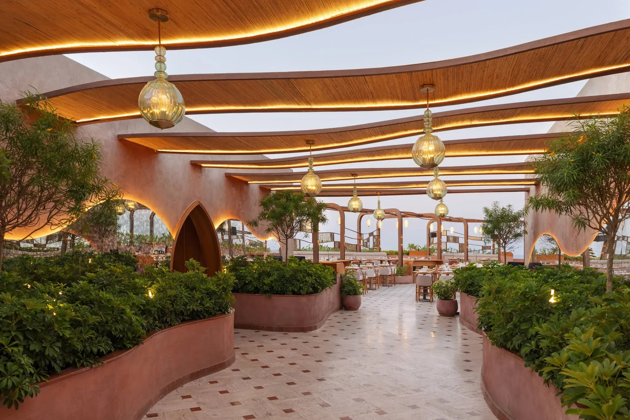 Planted walkway under a wavy timber canopy with hanging glass lanterns
