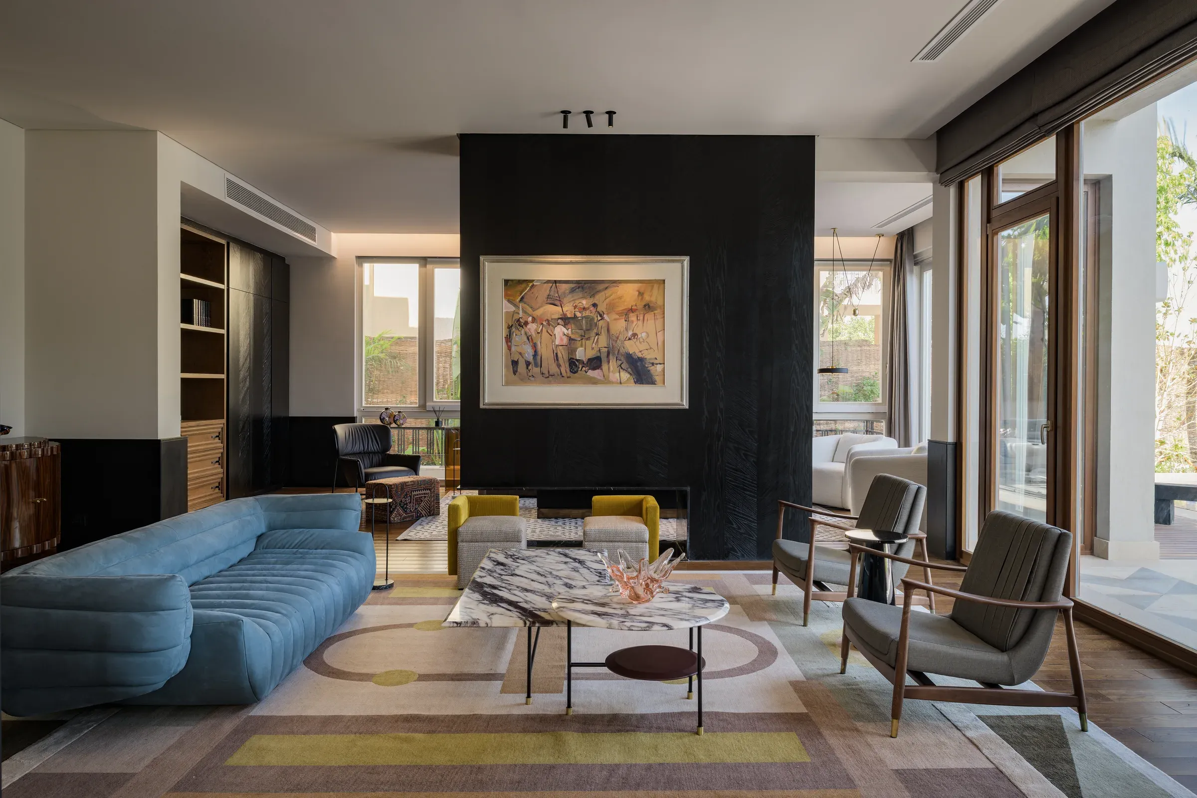 Living room with blue-grey curved sofa and black fireplace wall, pool beyond