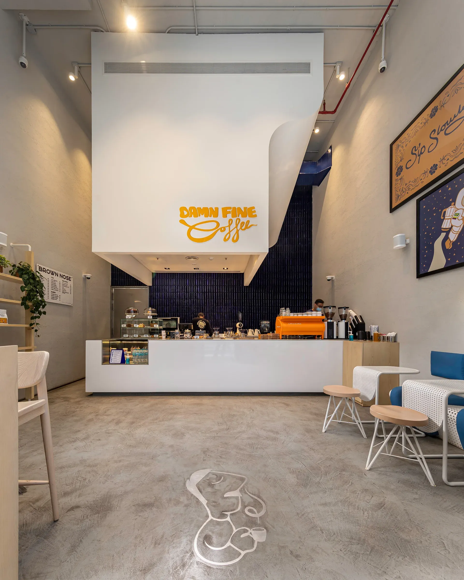 High-ceilinged coffee shop with white counter, blue tile wall and white bulkhead