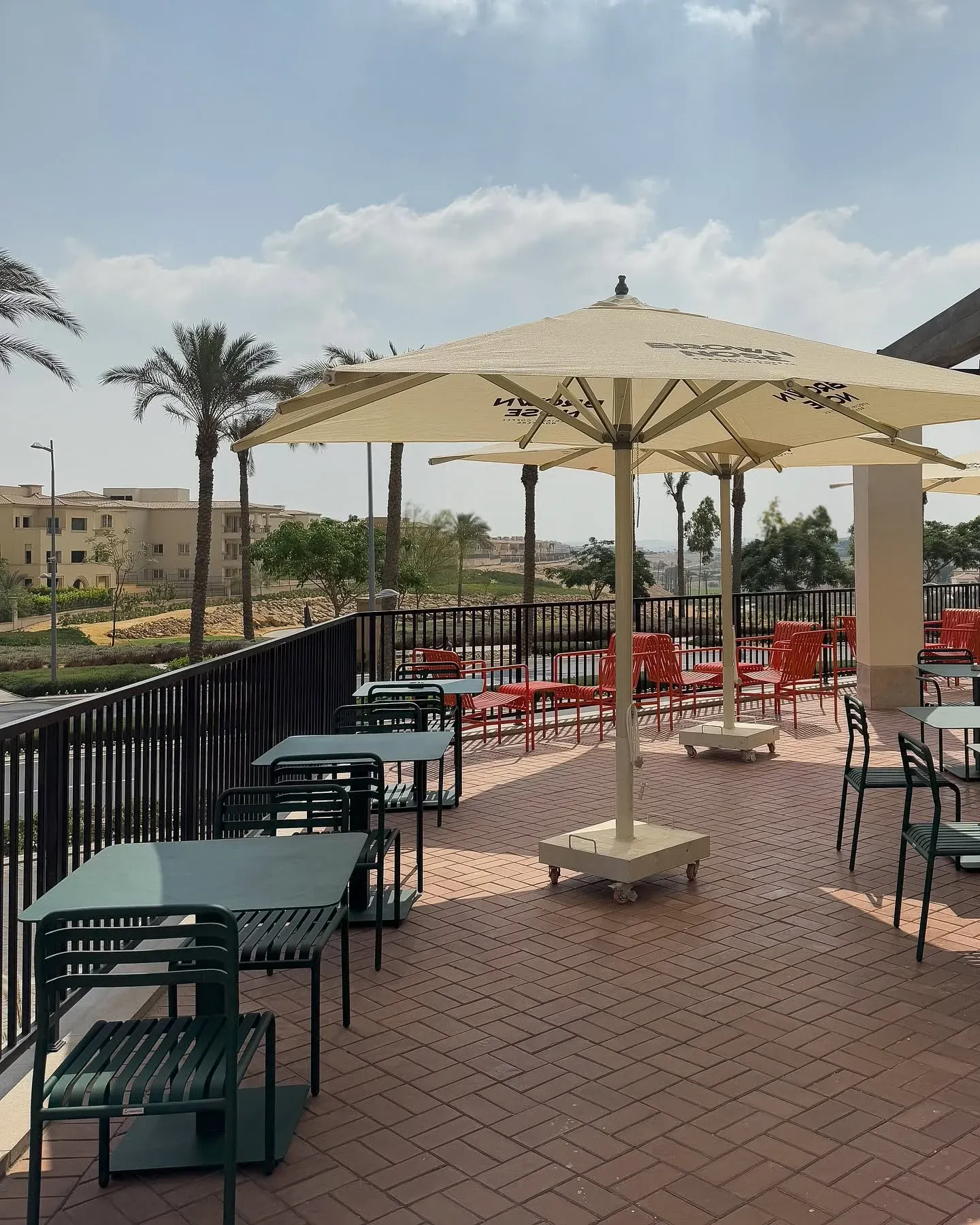 Terrace with cream parasols and green metal tables on brick paving