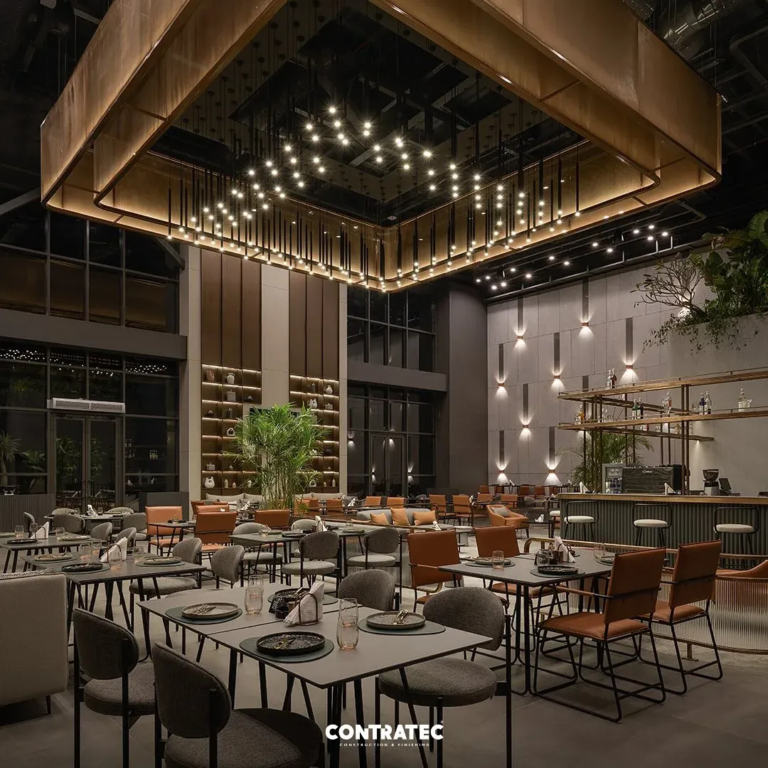 Set tables under the square brass light canopy, planters behind
