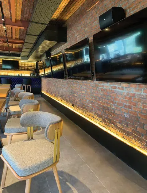 Padded chairs along a brick wall with a row of television screens