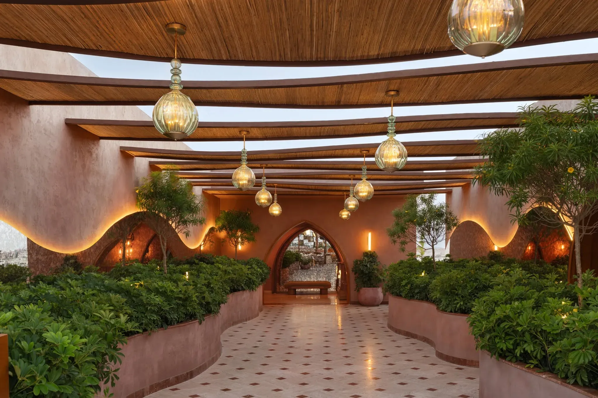Arched doorway at the end of a planted walkway under a lit timber canopy