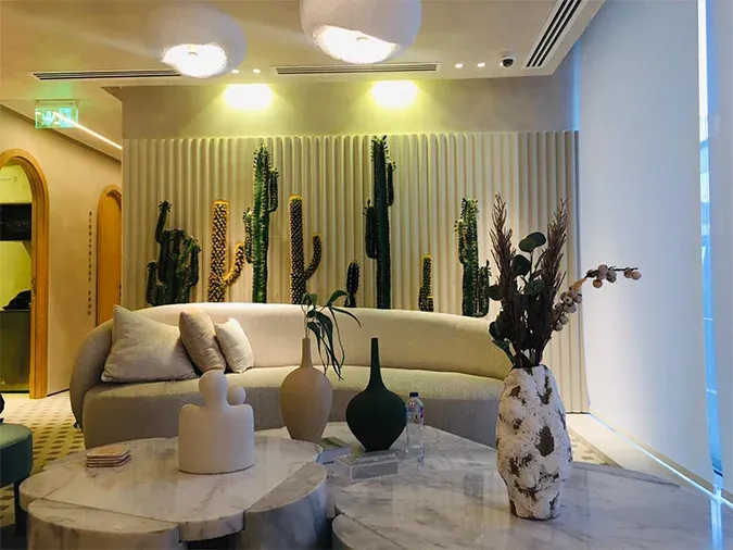 Curved cream sofa and marble tables in front of a fluted panel with cacti