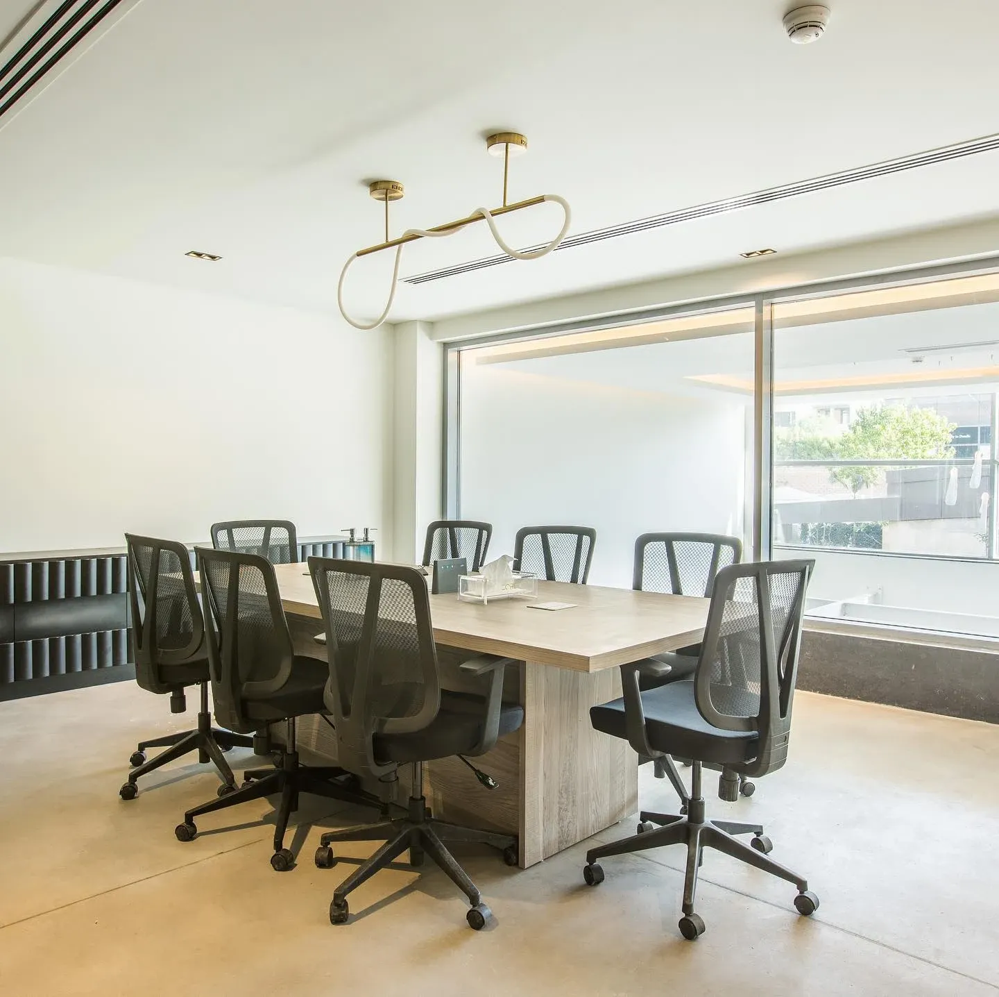 Meeting room with timber table, mesh chairs and a looped pendant light