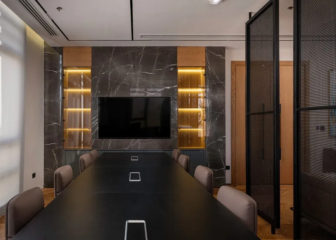 Boardroom table and stone-clad wall with lit shelves and a screen