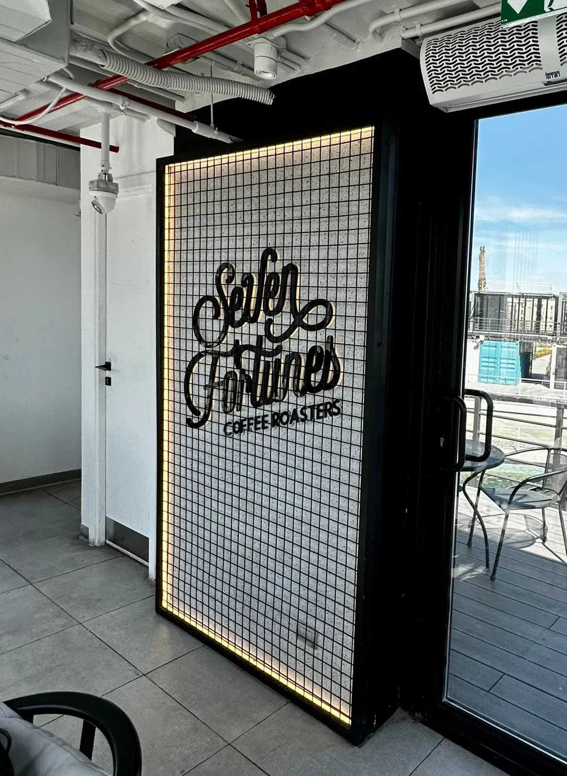 Illuminated mesh sign panel with the Seven Fortunes logo beside a glazed door