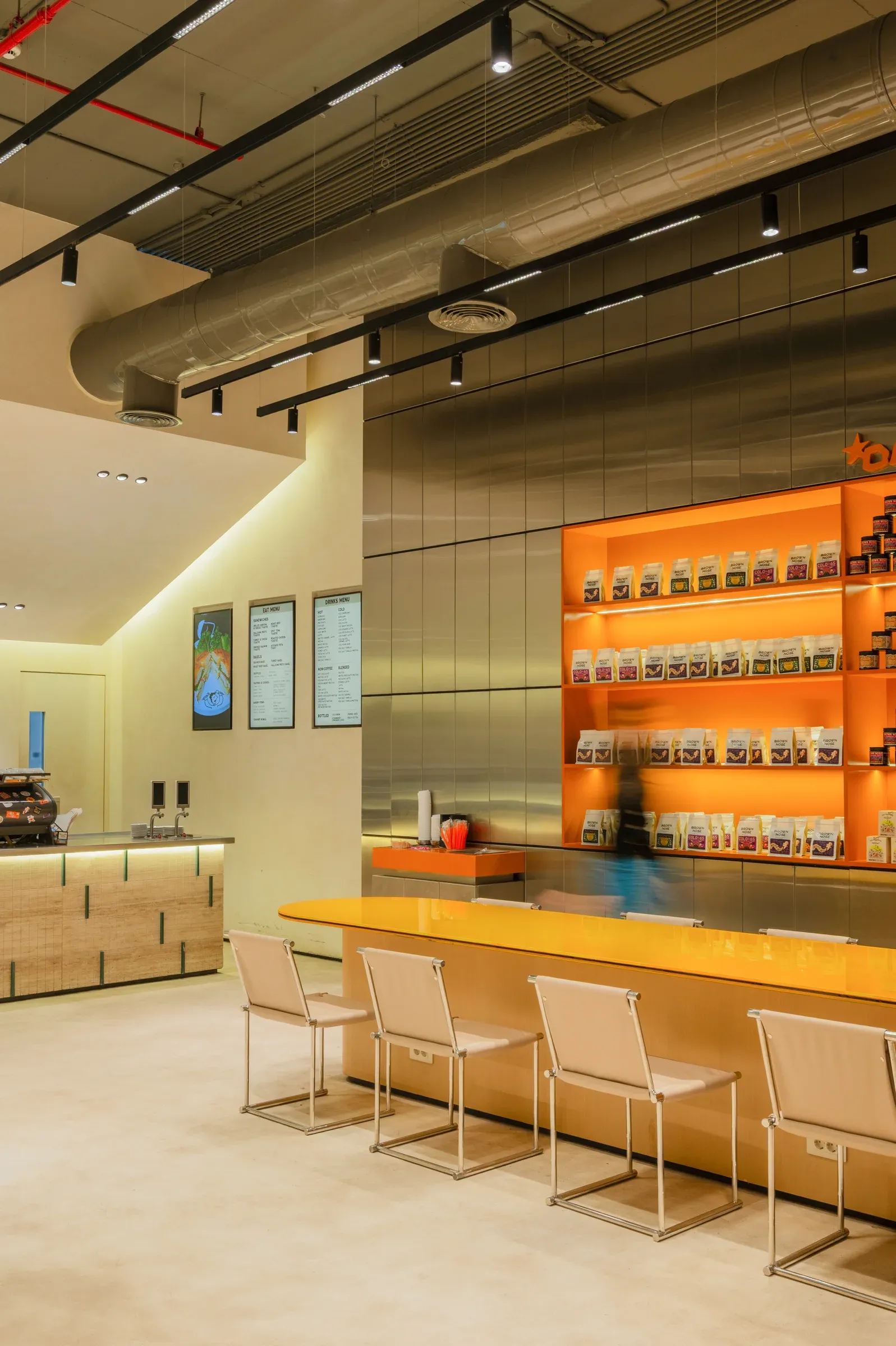 Yellow counter and chairs under exposed ceiling ducts and track lights