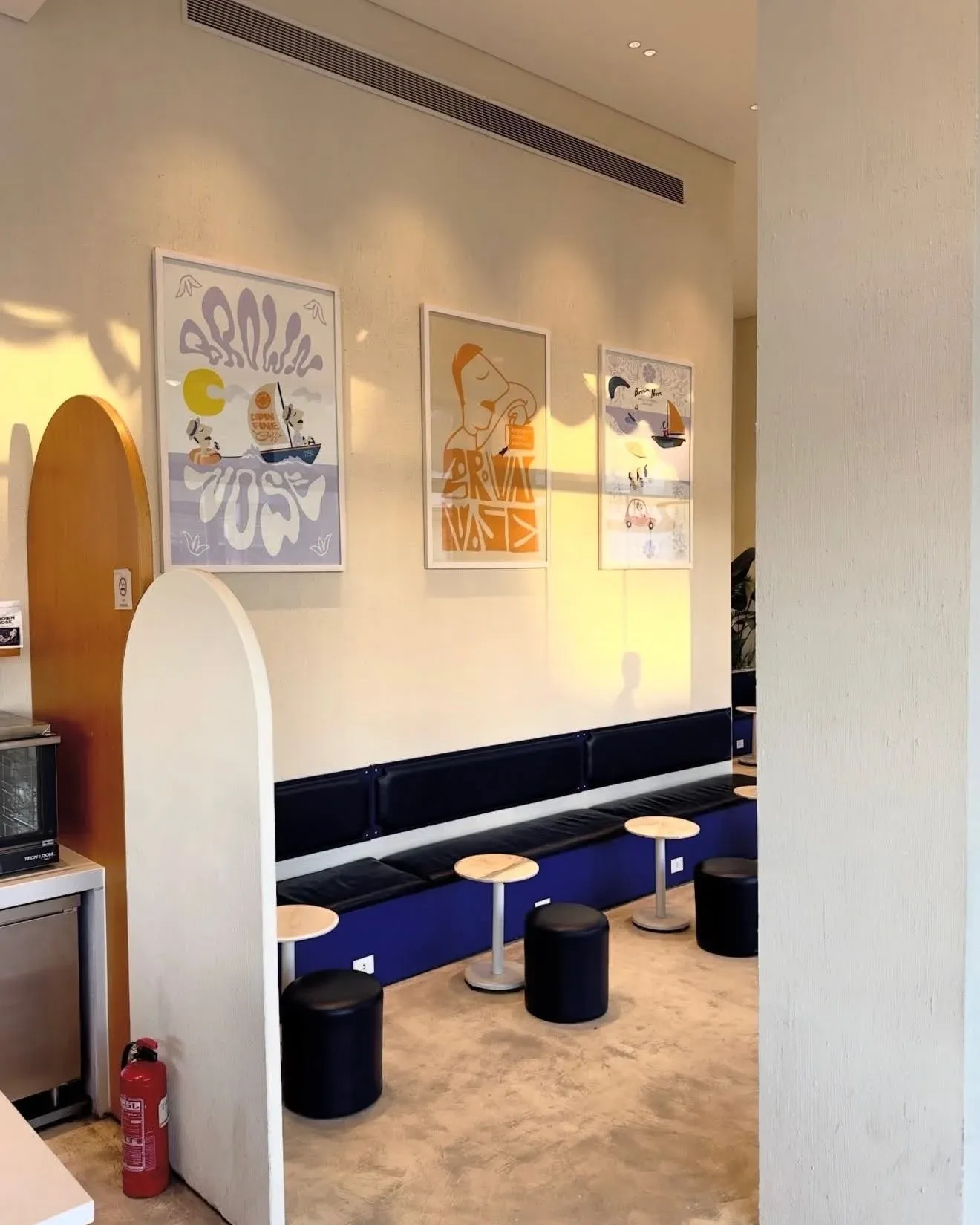 Framed posters above a blue banquette and round black stools
