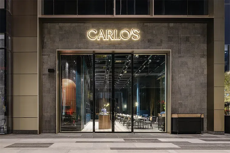 Carlo's glass entrance doors in stone cladding with a lit sign