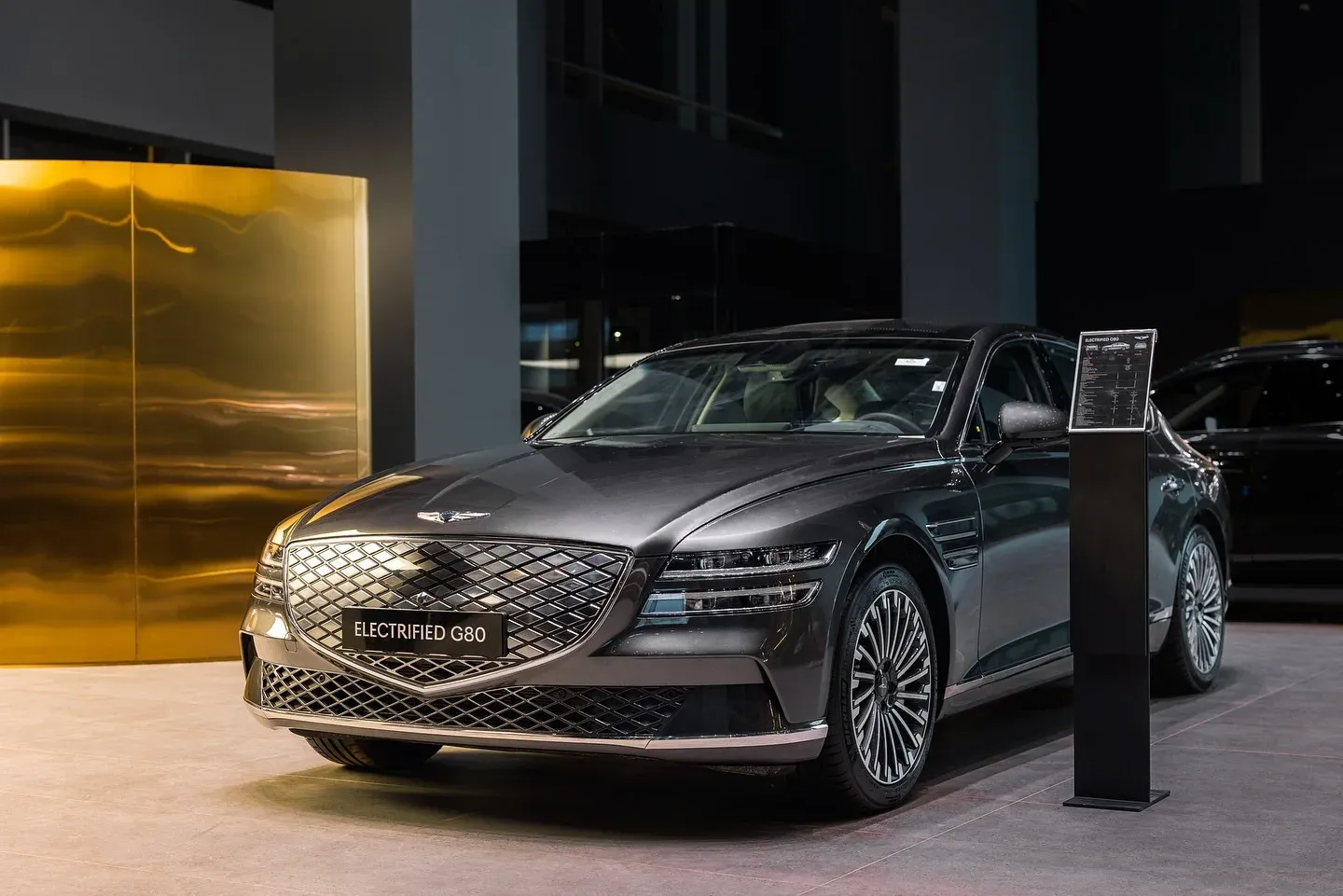 Dark sedan beside a brushed brass wall panel on the showroom floor