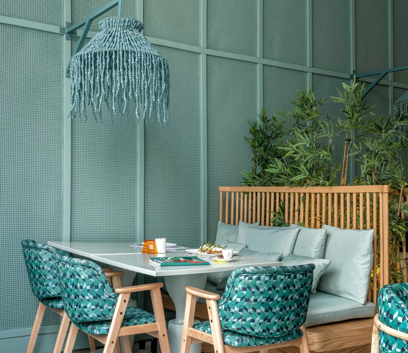 Sage green booth with teal patterned chairs and a fringed pendant light