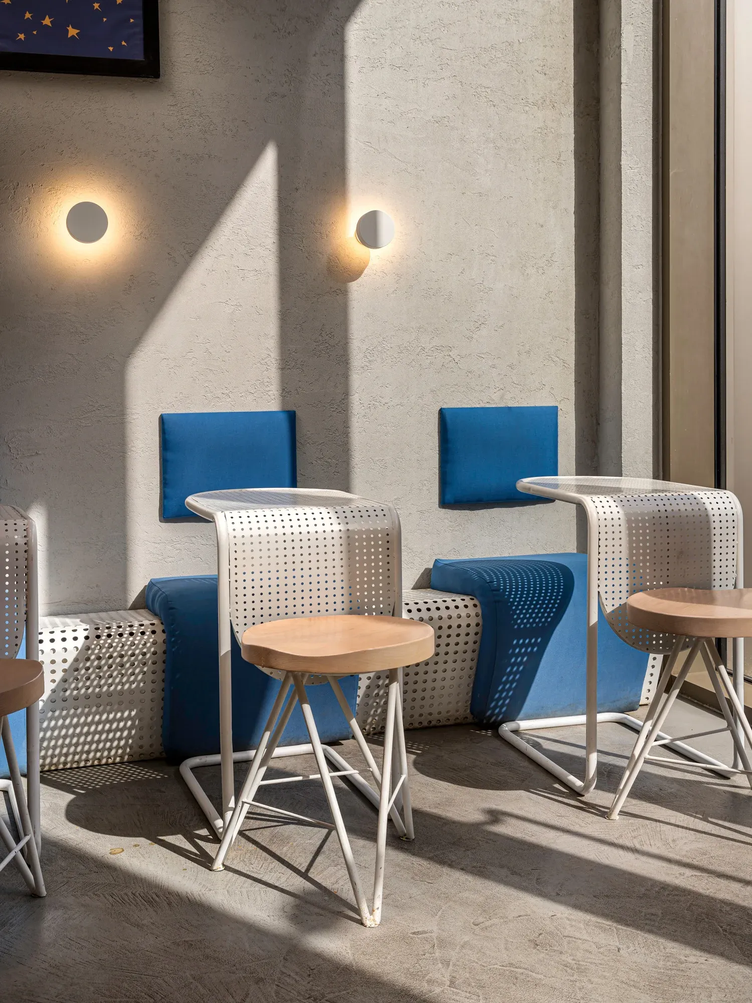 Blue upholstered stools and perforated white chairs beside the window