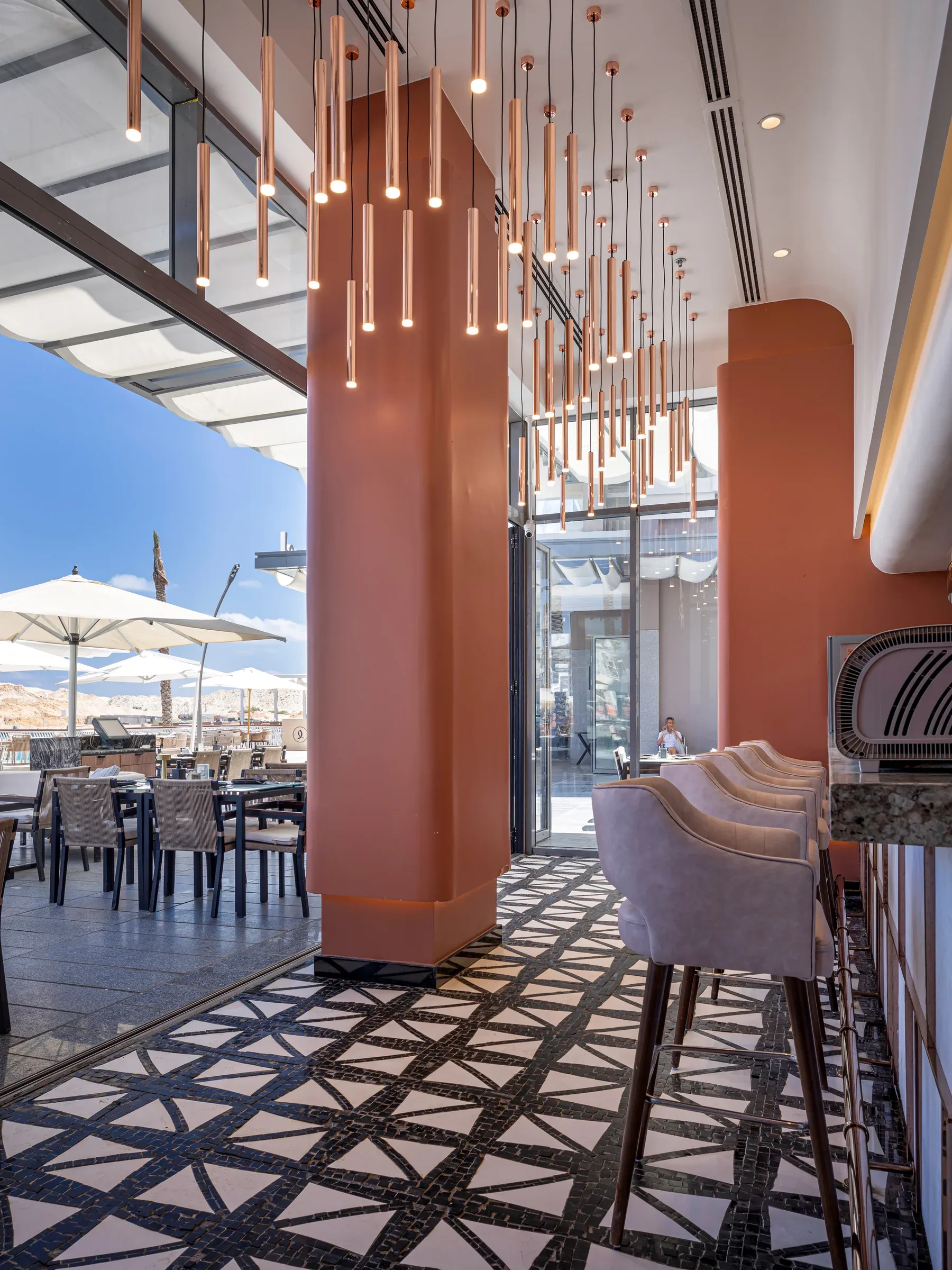 Bar stool and terracotta column opening onto a terrace with white umbrellas