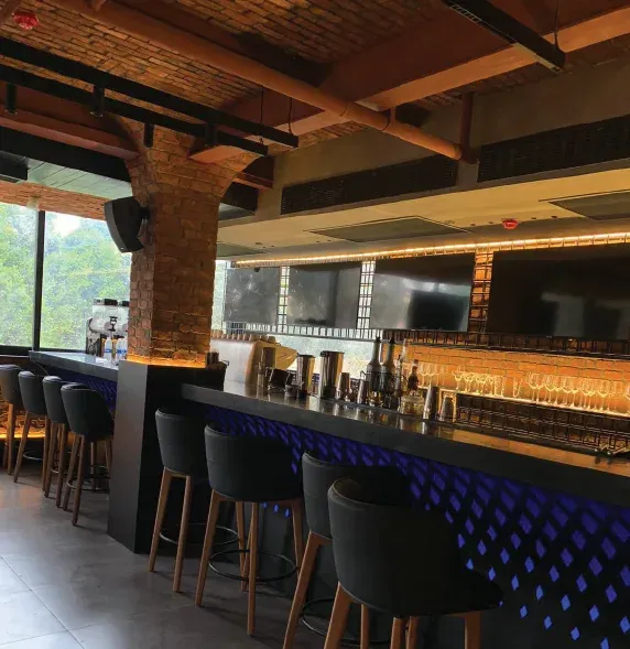 Bar counter with black stools, brick pillars and a glass-shelf back bar