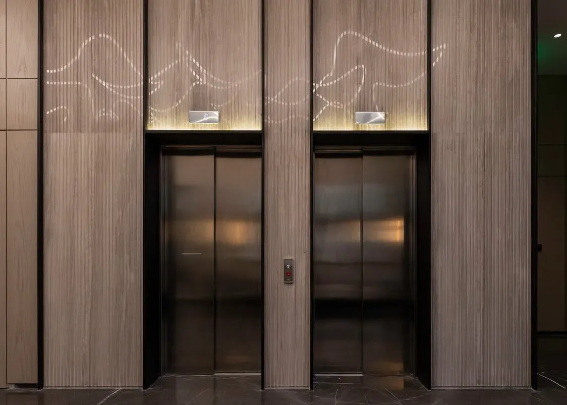 Two lifts framed by timber panelling with a lit line pattern above