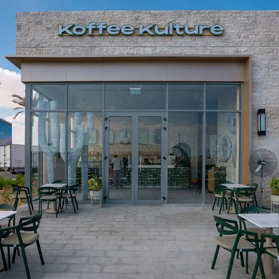 Entrance with Koffee Kulture sign and green terrace chairs