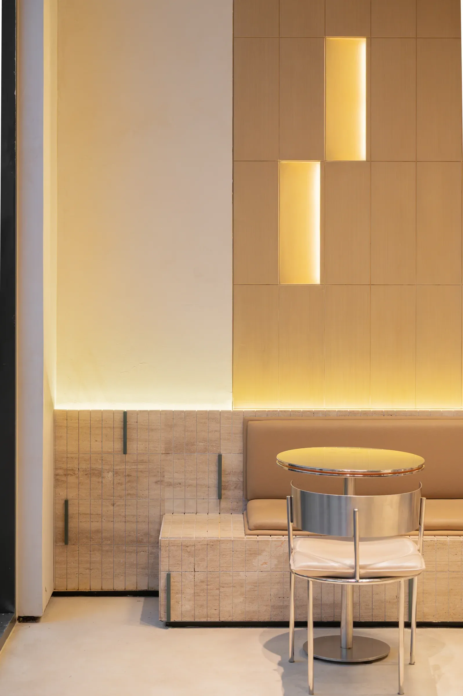 Round table and bench seat beside a wall of lit vertical slots