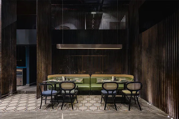 Green banquette and cane chairs against vertical timber slats on a hexagon-tile floor