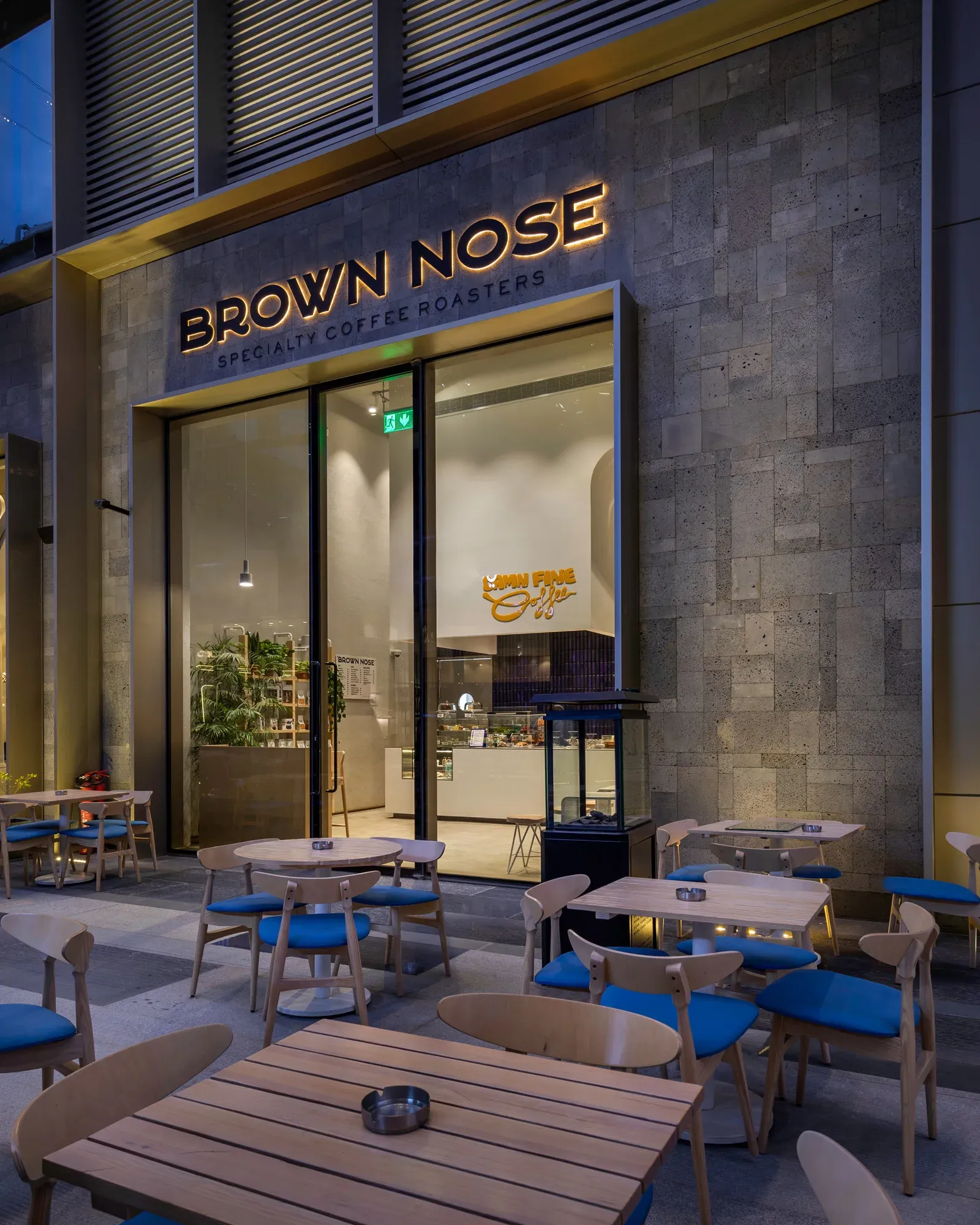 Glass storefront and sign with lit interior behind outdoor tables