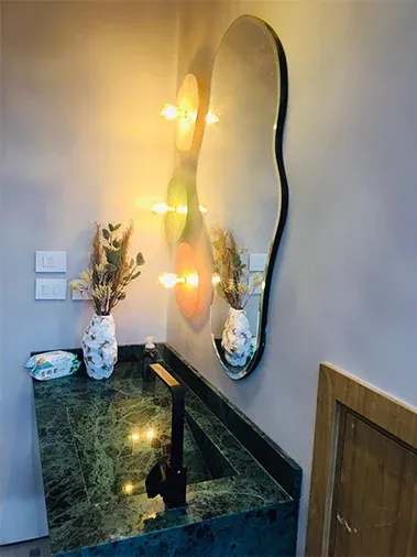 Green marble basin with a wavy mirror and wall lights