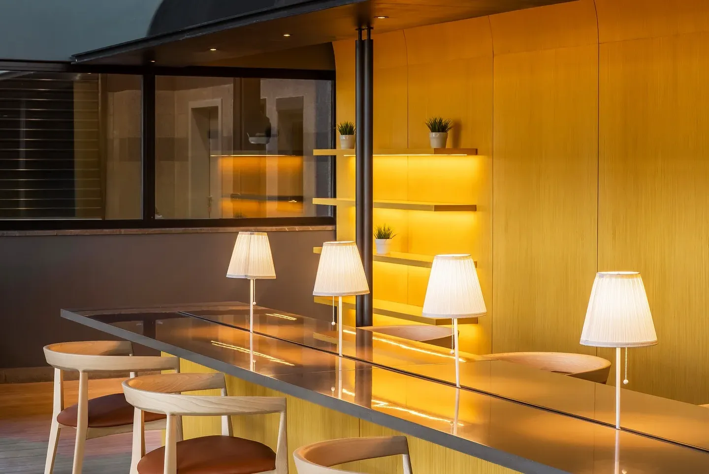 Communal table with fabric lamps in front of a curved yellow timber wall