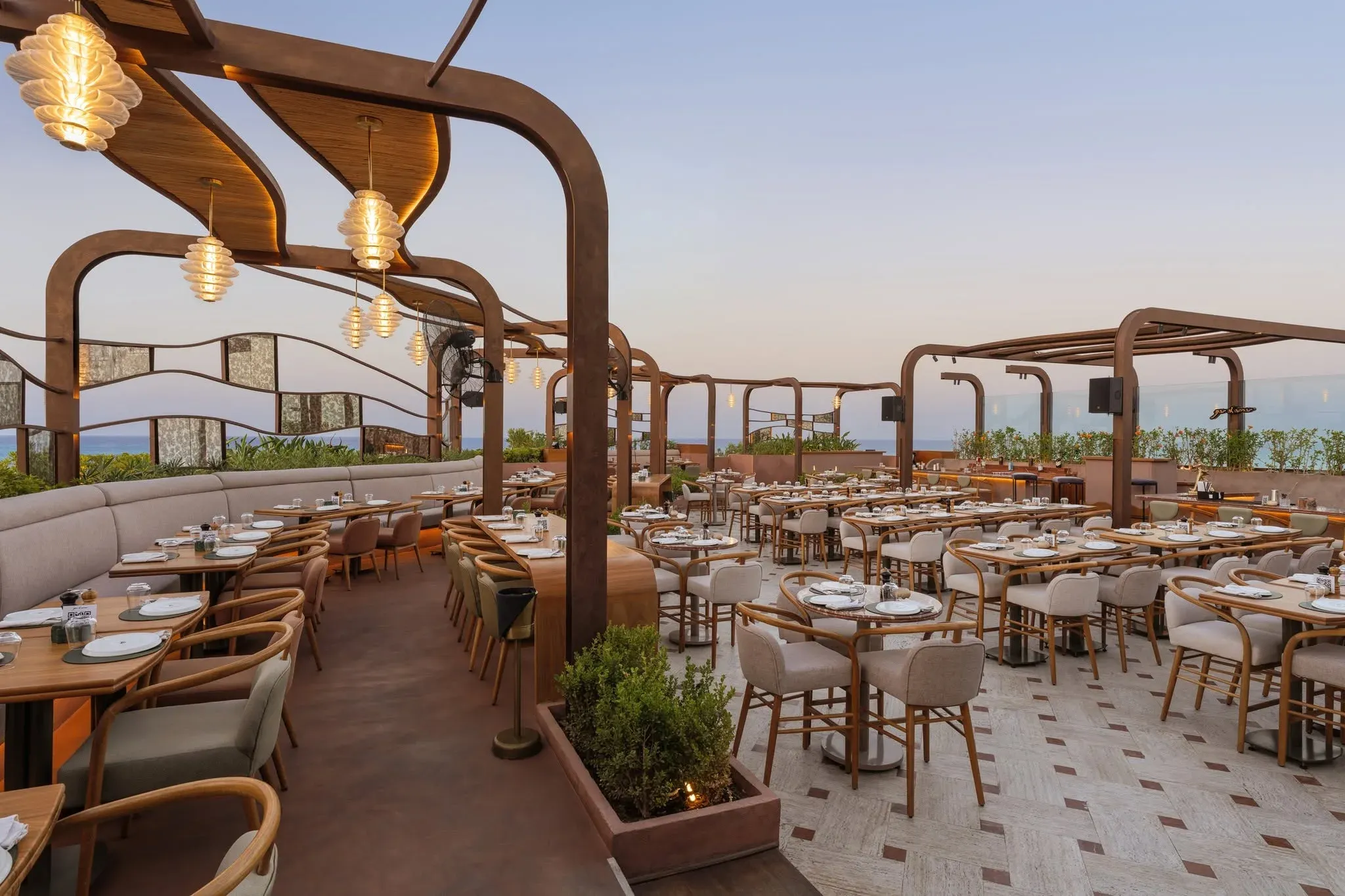Terrace dining with steel arches and banquette seating at dusk