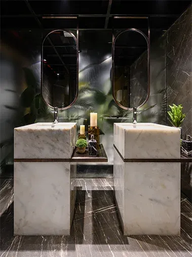 Twin marble washbasins with oval mirrors in a dark washroom