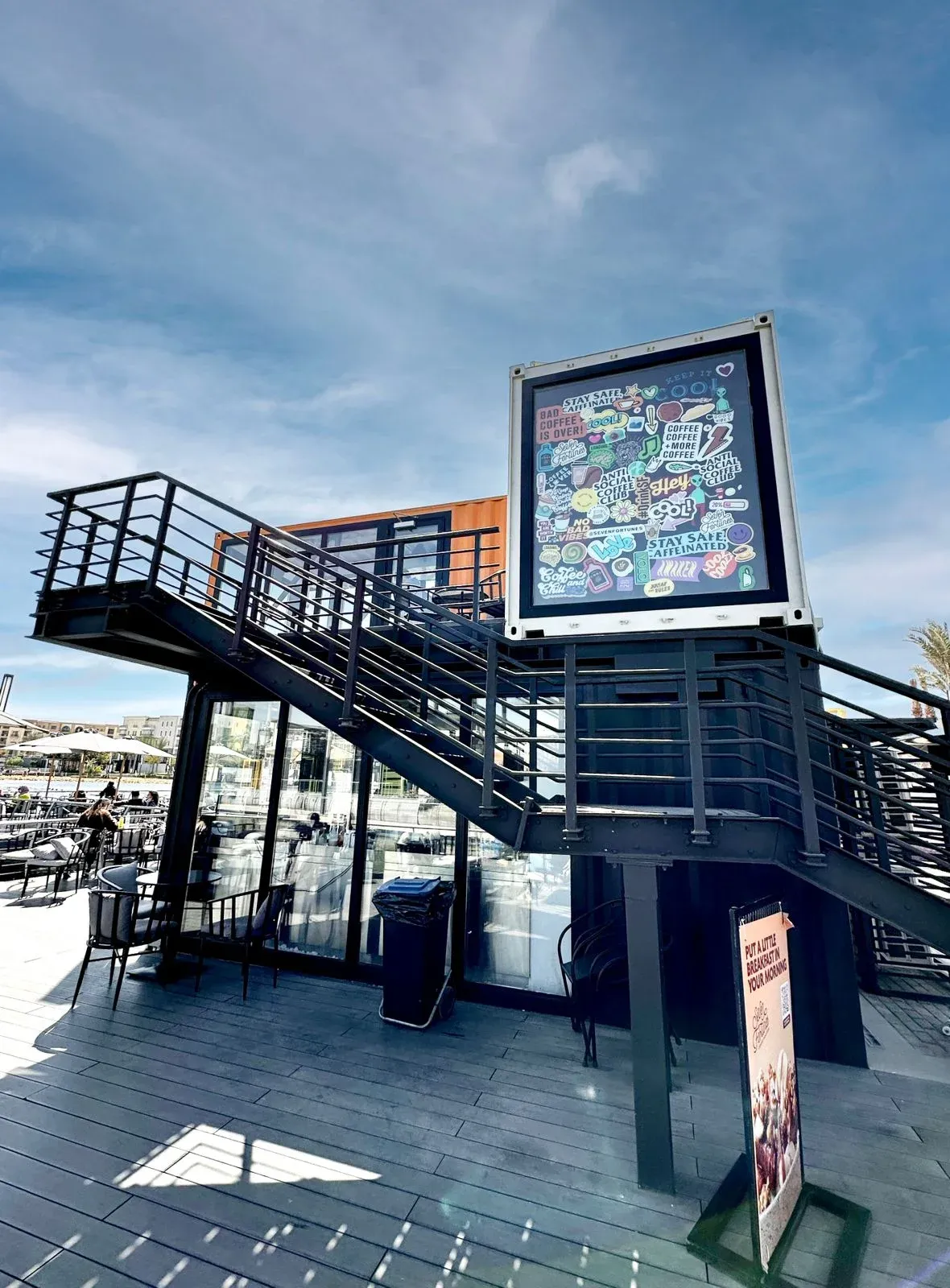 Cafe with steel stairs and an illustrated sign panel against the sky
