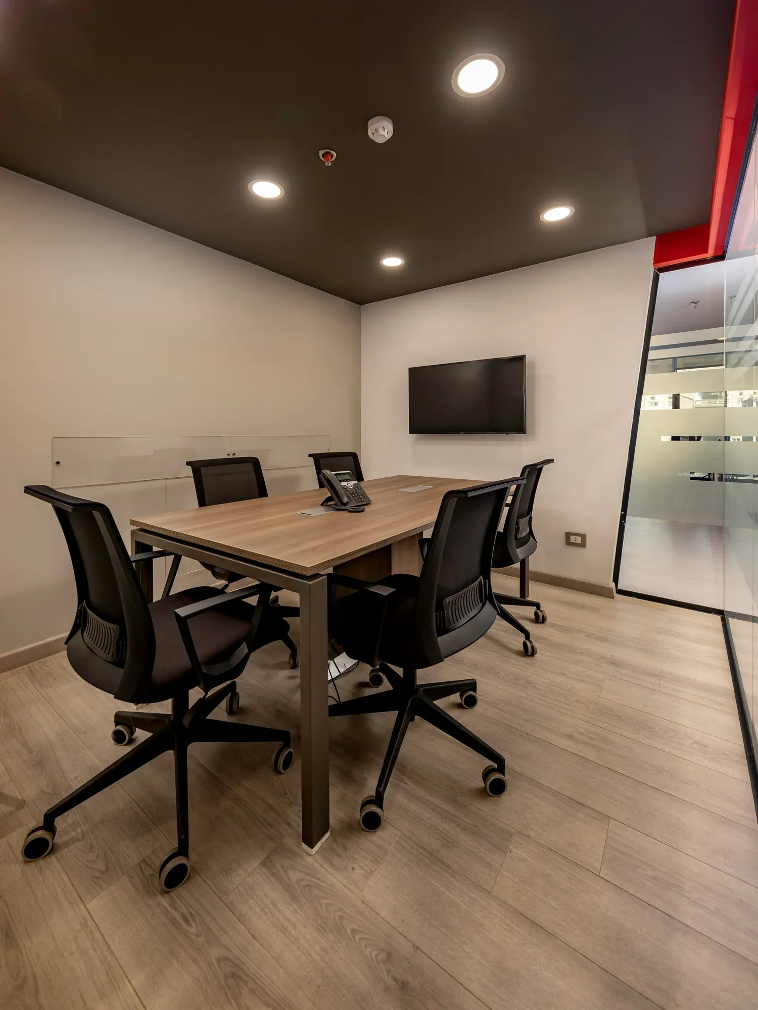 Small meeting room with timber table, black chairs and red accent wall