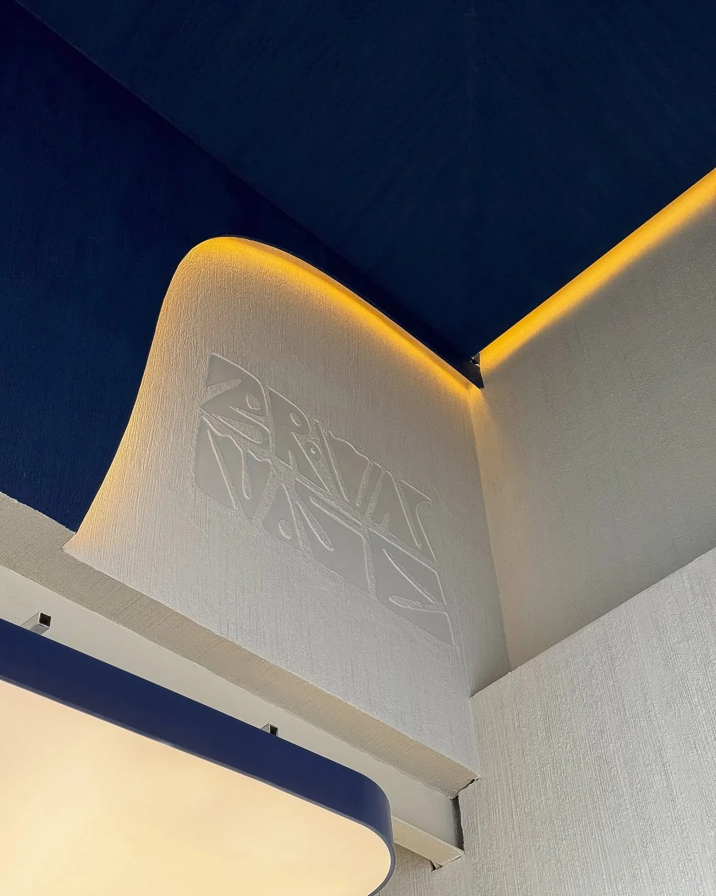 Curved white plaster feature with embossed pattern and lit blue ceiling edge