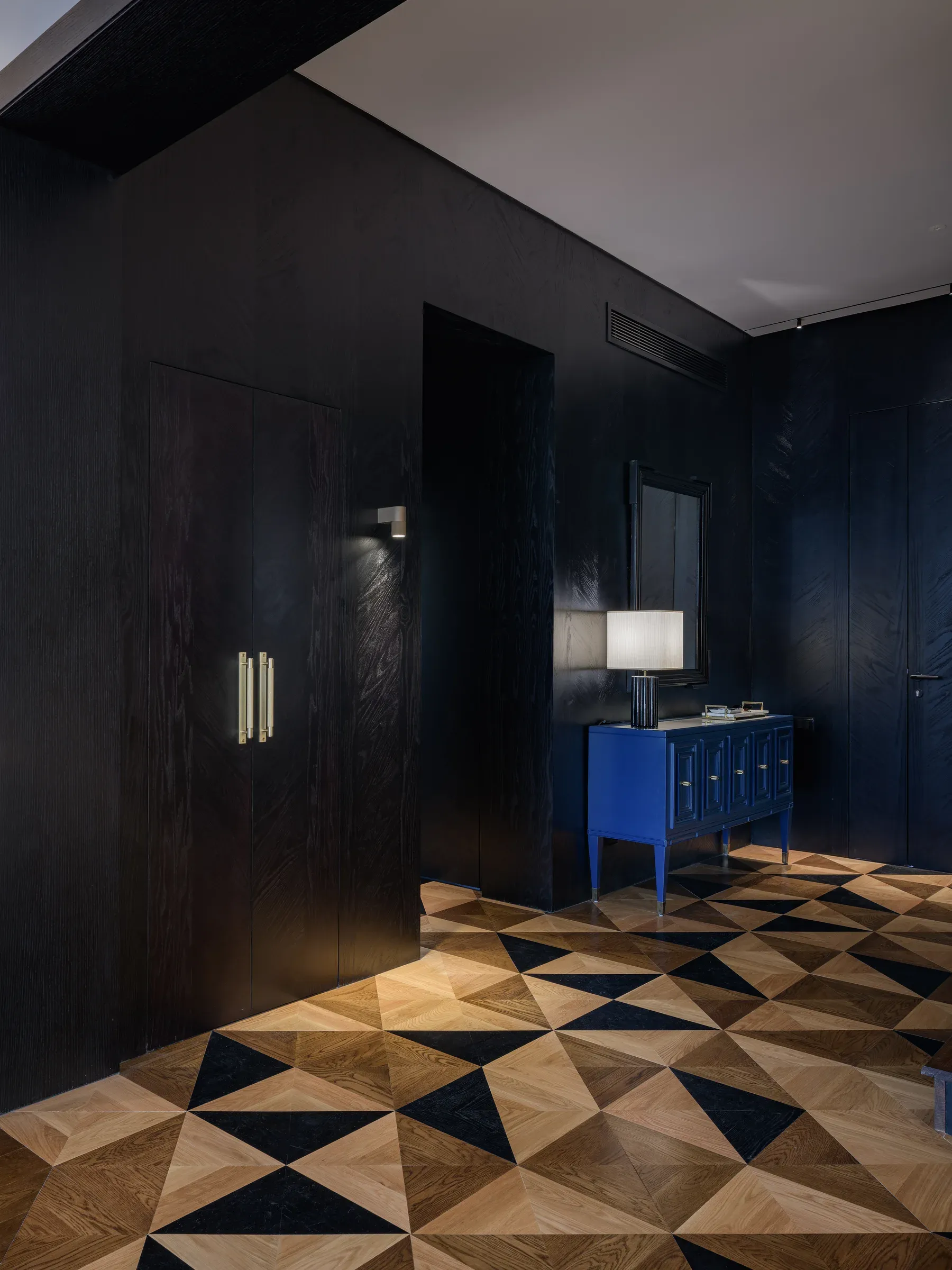 Entrance with geometric marquetry floor and a blue console against black panelling